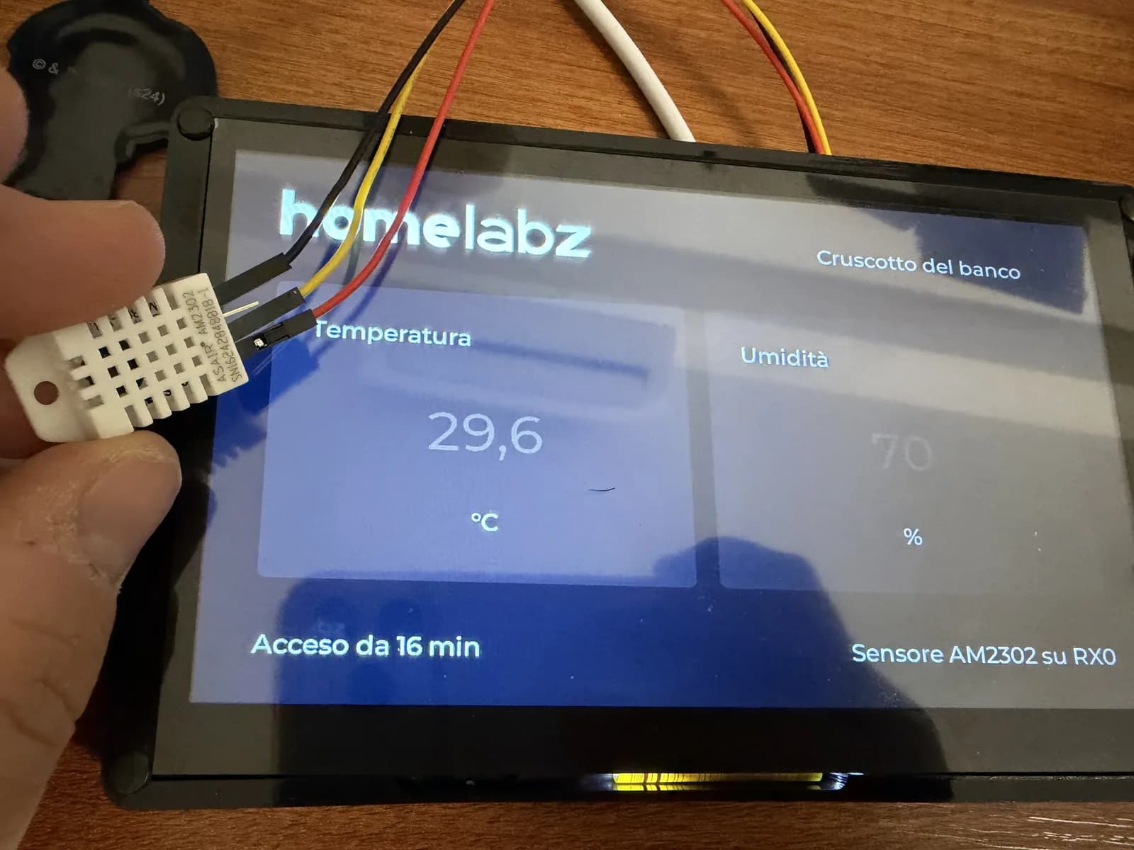 Il cruscotto homelabz sul CrowPanel Advance 7 con 29,6 °C e 70% di umidità, sensore AM2302 tenuto in mano e collegato alla porta UART0-OUT